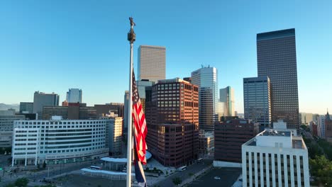 United-States-and-Colorado-flags-waving-in-front-of-Denver,-CO-skyline-during-golden-hour