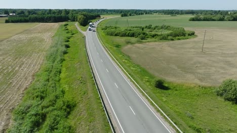 Aerial-establishing-shot-of-a-rural-landscape,-countryside-road-with-trucks-and-cars-moving,-lush-green-agricultural-crop-fields,-sunny-summer-day,-wide-drone-shot-moving-forward