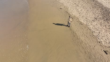 Woman-walking-alone-on-sandy-beach-during-calm-sunny-day,-solitude