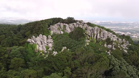 Rock-formation-on-forested-hillside-at-foggy-morning-in-Sintra,-Orbiting-shot
