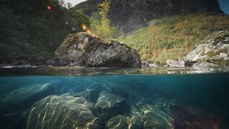 Slow-motion-shot-of-rocky-underwater-of-Loen-lake-in-Vestland,-Norway-with-mountain-range-in-the-background-on-a-sunny-day