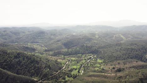 Toma-De-Drones-De-Un-Paisaje-Montañoso-Bañado-Por-El-Sol-Con-Plantaciones,-Campos-Y-árboles.