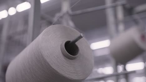 Close-up-shot-of-high-tech-machinery-in-factory-weaving-material-on-reels-of-thread