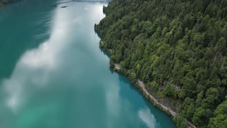 Aerial-arc-shot-of-Klontalersee-lake-turquoise-waters-reflecting-clouds