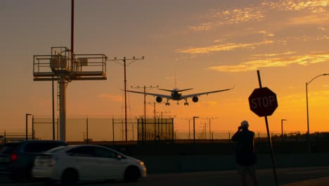 Man-filming-a-two-engine-silhouetted-passenger-plane-landing-in-LAX-Los-Angeles-at-sunset