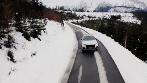 Weißes-Auto-Fährt-Im-Winter-Auf-Verschneiter-Bergstraße---Drohnenaufnahme