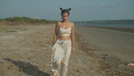 Cinematic-shot-of-an-indian-fashion-model-wearing-a-white-and-colored-trousers-and-top-walking-on-a-sandy-beach-on-a-wind-and-sunny-day-in-Goa,-India