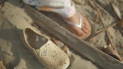 Cinematic-shot-of-an-indian-fashion-model-stepping-with-sandals-next-to-an-old-shoe-on-a-sandy-beach-in-Goa-India