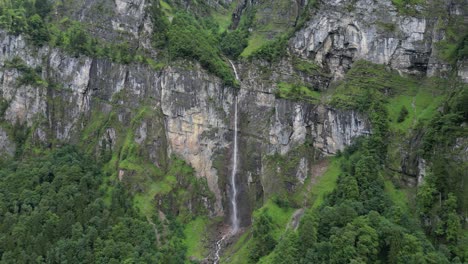 Hermosa-Cascada-Que-Cae-Desde-Terreno-Rocoso-De-Los-Alpes-Suizos,-Antena