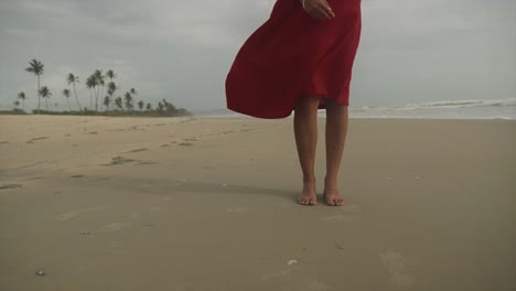 Cinematic-shot-of-an-indian-fashion-model-wearing-a-red-dress-standing-on-a-sandy-beach-in-Goa,-India-on-a-Windy-Day