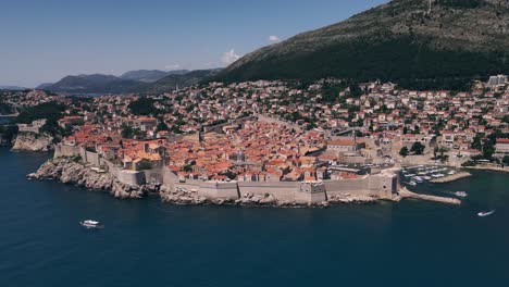 Wide-aerial-drone-shot-of-the-walled-city-of-Dubrovnik,-Croatia-slowly-pulling-back-to-reveal-the-entire-city-and-surrounding-landscape-with-boats-on-the-Adriatic