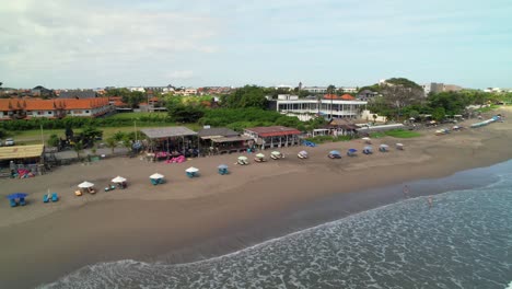 Row-Of-Beach-Bars-and-Cafes-Along-Winding-Batu-Belig-Beach-Coastline,-Parasols-and-Deckchairs-Spread-Evenly-in-Line,-Bali-Indonesia---Aerial-parallax