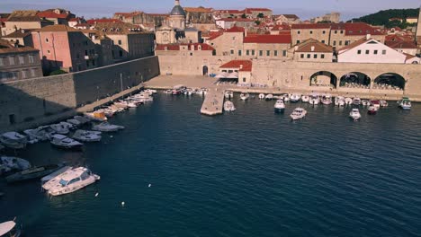 Aerial-drone-shot-starting-close-on-the-boats-in-the-port-of-Dubrovnik,-Croatia-and-pulling-back-to-reveal-the-entire-walled-city