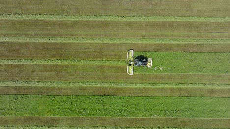 Aerial-establishing-view-of-a-tractor-mowing-a-fresh-green-grass-field,-a-farmer-in-a-modern-tractor-preparing-food-for-farm-animals,-sunny-summer-day,-wide-descending-birdseye-drone-dolly-shot