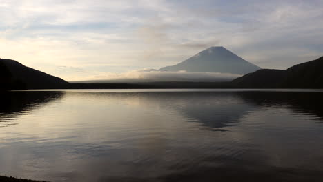 Im-Sanften-Ersten-Licht-Schwenkt-Die-Kamera-Und-Gibt-Den-Blick-Auf-Die-Spiegelglatte-Oberfläche-Des-Motosu-Sees-Frei,-Die-Die-Heitere-Erhabenheit-Des-Berges-Fuji-Widerspiegelt