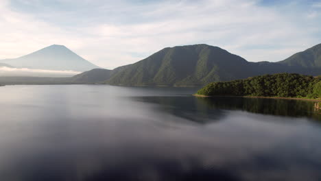Aerial-view-Lake-Motosu-gleams-below,-as-the-camera-tilts,-revealing-the-majestic-Mount-Fuji-on-the-horizon