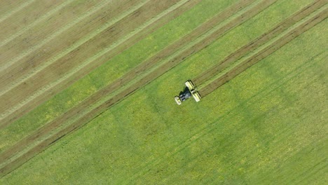 Aerial-birdseye-view-of-a-tractor-mowing-a-fresh-green-grass-field,-a-farmer-in-a-modern-tractor-preparing-food-for-farm-animals,-sunny-summer-day,-wide-descending-drone-dolly-shot-moving-left