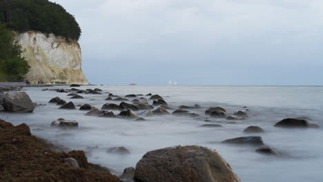 Timelapse-of-People-Tourists-Walk-Along-White-Chalk-Cliffs-on-Rugen-Island-while-Baltic-Sea-Waves-Crash-Rolling-Over-Stony-Beach