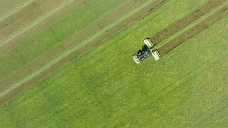Aerial-birdseye-view-of-a-tractor-mowing-a-fresh-green-grass-field,-a-farmer-in-a-modern-tractor-preparing-food-for-farm-animals,-sunny-summer-day,-wide-drone-dolly-shot-moving-left