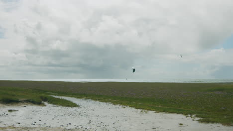 Super-wide-shot-of-kite-surfer-at-the-north-sea,-small-part-of-sand-beach-in-the-foreground,-grass-in-the-middle-ground