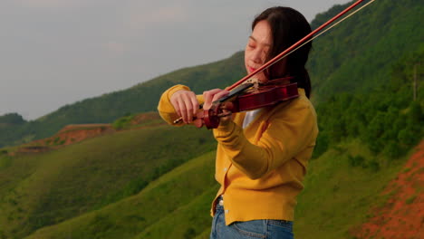 Slow-Motion-of-Woman-playing-violin-in-nature,-green-hills-in-background