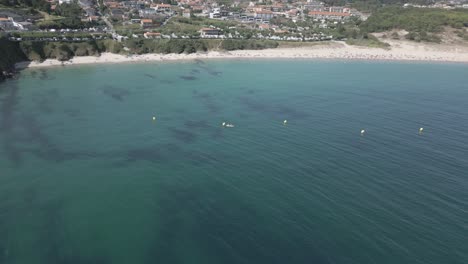 Rohaufnahmen-Eines-überfüllten-Strandes-In-Einem-Küstendorf-Mit-Türkisfarbenem,-Klarem-Wasser