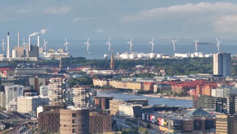 Scenic-aerial-of-wind-turbines,-seaside-industrial-zone-and-commercial-buildings-in-Copenhagen,-Denmark