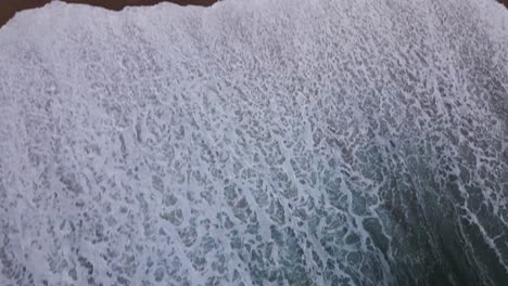 Eine-Ungewöhnliche-Draufsicht-Auf-Die-Wellen-Des-Ungezähmten-Ozeans,-Die-über-Einen-Sandstrand-Spülen