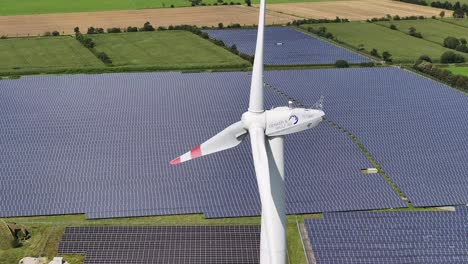 Eine-Windkraftanlage-Steht-In-Der-Mitte-Eines-Solarfeldes,-Umgeben-Von-Sonnenkollektoren,-Langsame-Drohnenumlaufbahn