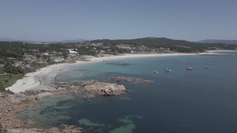 Raw-Aerial-Shot-of-Rocky-Shore-and-Beach-with-Clear-Water-with-Sailboats