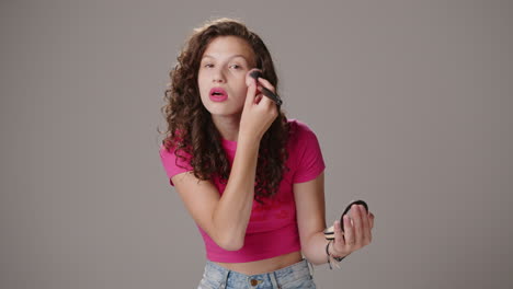 Smiling-young-attractive-brunette-with-pink-shirt-applies-makeup-with-brush