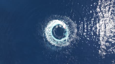 Drone-Shot-of-Boast-Spinning-in-Circles-in-Blue-Sea-Water,-Top-Down-Aerial-View-50fps