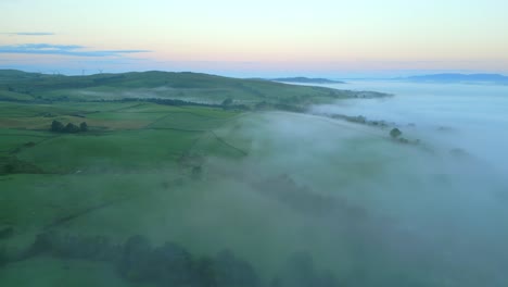 Flying-over-English-patchwork-fields-with-misty-fog-bank-at-sunrise