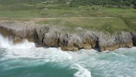 Aerial-parallax-around-crashing-waves-on-rocky-limestone-cliffs,-bufones-de-pria-asturias-spain,-slow-motion