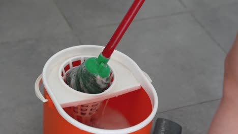 Top-down-close-up-slow-motion-of-a-red-bucket-as-the-wet-mop-is-wrung-out-in-preparation-for-house-cleaning