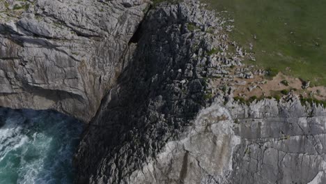 Jagged-eroded-limestone-cliffs-to-grassy-green-hills-of-bufones-de-pria-asturias-spain,-aerial-tilt-up