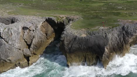 Explorers-roam-on-lush-green-grassy-flats-above-bufones-de-pria-asturias-spain-sea-cliffs