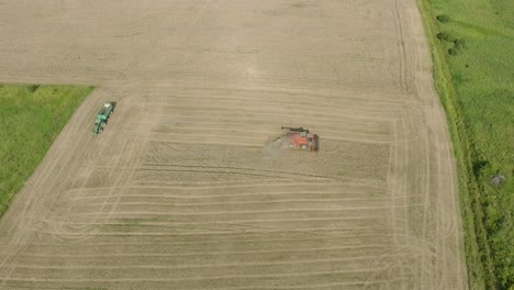 Aerial-establishing-view-of-combine-harvester-mowing-yellow-wheat,-dust-clouds-rise-behind-the-machine,-food-industry,-yellow-reap-grain-crops,-sunny-summer-day,-drone-shot-moving-forward,-tilt-down