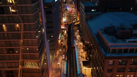 Aerial-view-overlooking-a-L-train-driving-in-middle-of-buildings-in-illuminated-Chicago,-USA