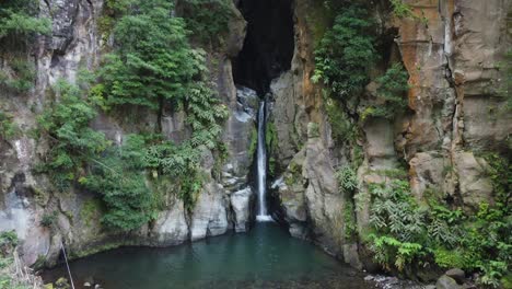 Narrow-waterfall-flows-out-of-slot-canyon-at-Salto-do-Cabrito,-Azores