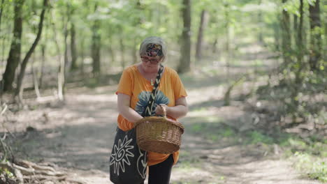 Medium-shot-of-Fat-Old-Women-with-grey-Hair-and-orange-T-shirt-looking-into-the-wooden-basket-in-the-middle-of-a-green-Forest-during-a-sunny-day-in-slow-motion-with-blurry-background