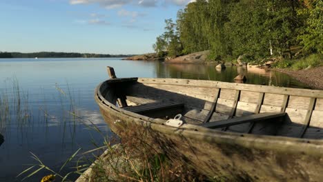 Wooden-rustic-boat-by-calm-water-sea-bay,-idyllic-nature-in-Finland,-crane-shot