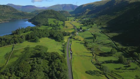 Valley-road-snaking-through-lush-green-countryside-beside-lake-and-surrounded-by-mountains-on-sunny-summer-morning-at-Thirlmere,-English-Lake-District,-Cumbria,-UK