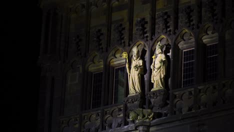 Dos-Estatuas-De-Santos-Se-Iluminan-En-El-Centro-De-Un-Edificio-Gótico-Obispos-Sosteniendo-Un-Bastón-Dorado-En-Medio-De-La-Noche-Praga,-República-Checa-Arquitectura-Esculturas-De-Arquitectura-Religiosa