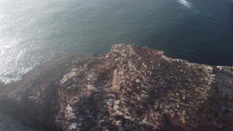 Drone-flyover-Rock-formation-with-foggy-clouds-in-atlantic-ocean,-tilt-down-shot