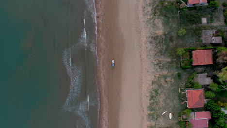 Aerial-top-down-shot-of-one-car-driving-along-an-empty-sandy-beach