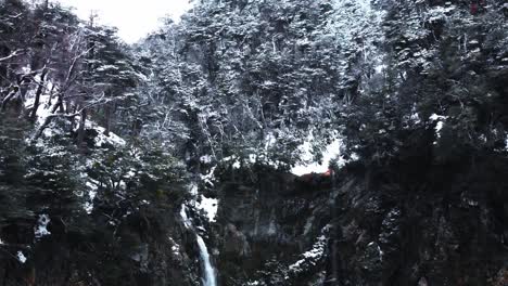 Slow-aerial-shot-of-a-snowy-mountain-forest-crossed-by-a-waterfall