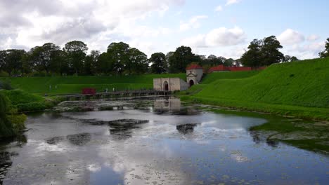 People-crossing-a-bridge-to-Kastellet-fortress-gate-next-to-a-pond-with-sky-reflection,-Copenhagen