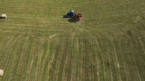Tractor-At-Work-Producing-Round-Hay-Bales-In-Oronoco,-Minnesota,-USA---aerial-drone-shot