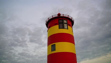 Red-yellow-small-Otto-Waalkes-lighthouse-in-front-of-an-overcast-sky-with-thick-clouds-in-the-evening